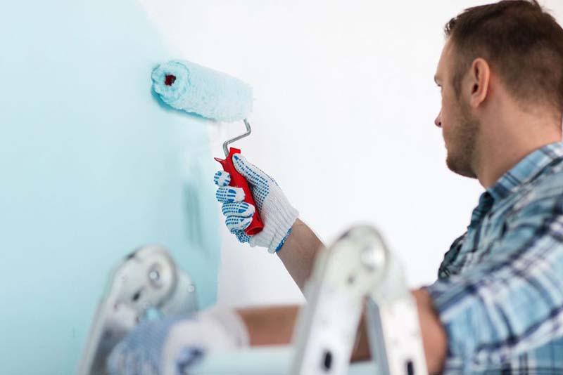 Man in painting overalls using a roller to paint a wall blue